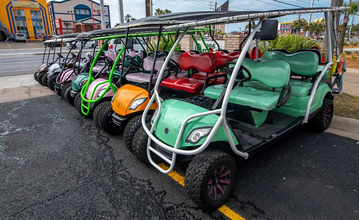 A series of brightly colored Paradise Fun Rentals golf carts parked in an organized manner in a parking lot.
