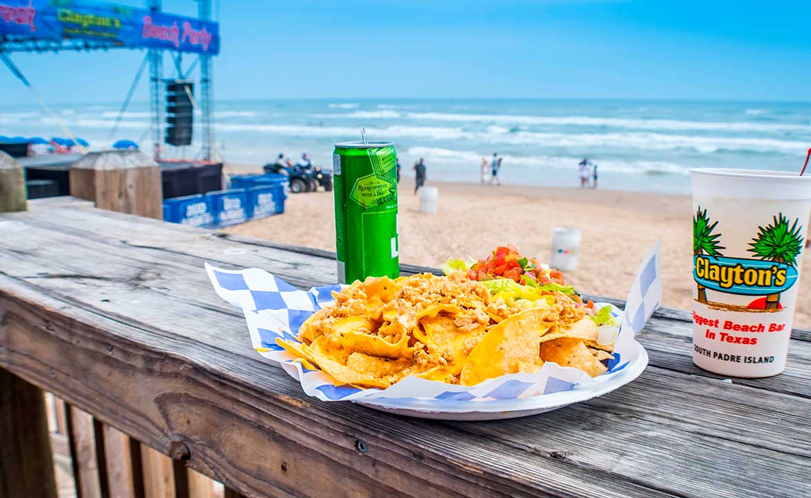 Biggest Beach Bar in Texas: Claytons in South Padre Island. A serving of crispy fries alongside a beverage on a wooden table surface.