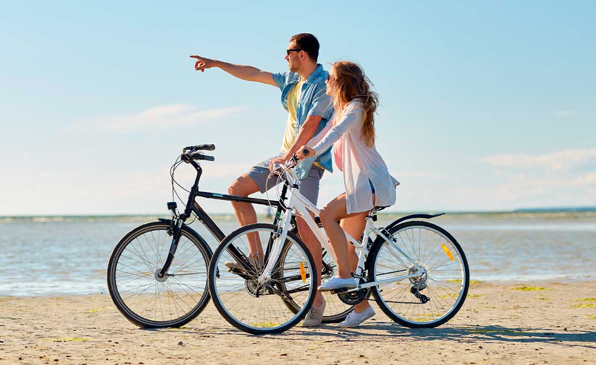 A man and woman ride bicycles along the beach on South Padre Island, enjoying sunny weather and ocean views.