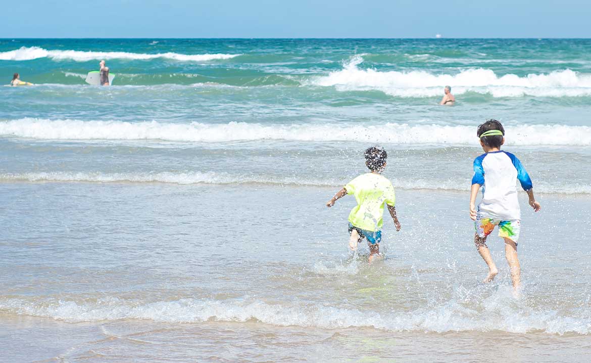 Two children excitedly sprinting into the waves at South Padre Island beach, enjoying a day of fun in the sun.