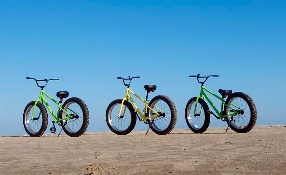 Three bicycles parked on a sandy beach at South Padre Island, with the Laguna Madre bike trails in the background.