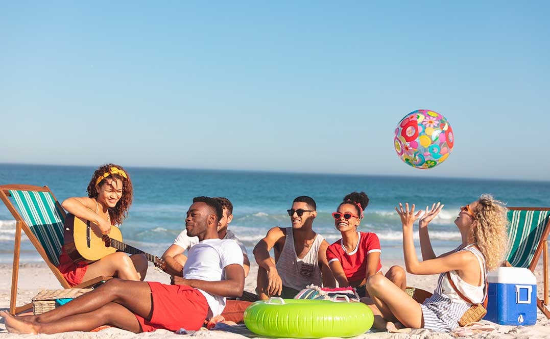Friends laughing and relaxing on the beach at South Padre Island, with the ocean in the background and clear blue skies.
