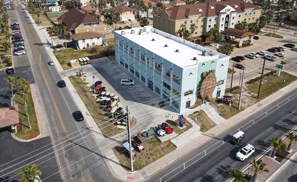Overhead view of a building in South Padre Island, featuring parked cars on the street, highlighting transportation tips for groups.
