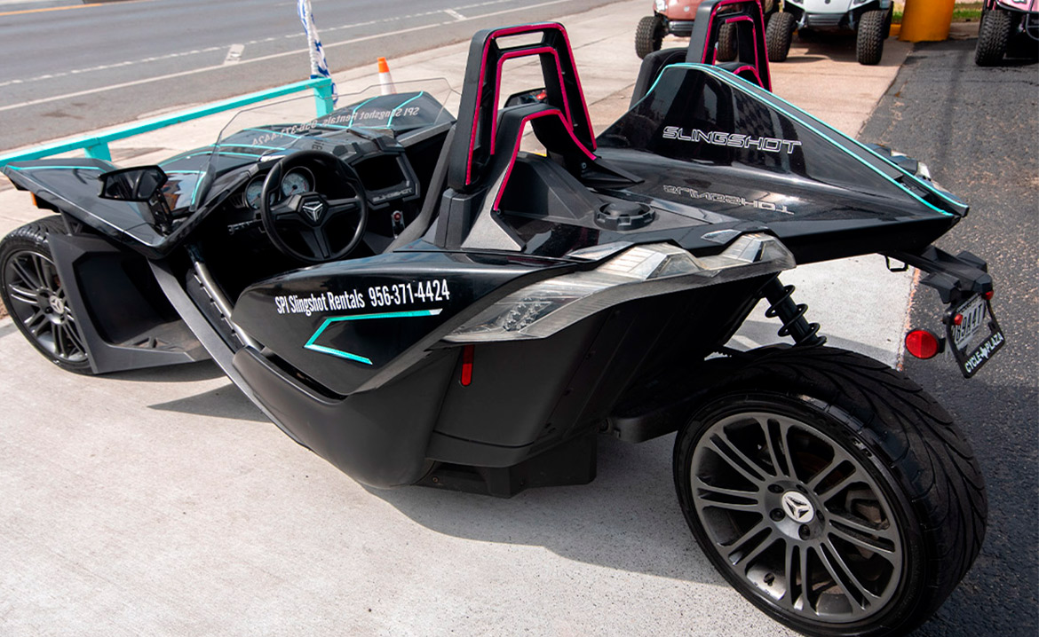 A black and pink motorcycle parked along the road, advertising slingshot rentals in South Padre Island.