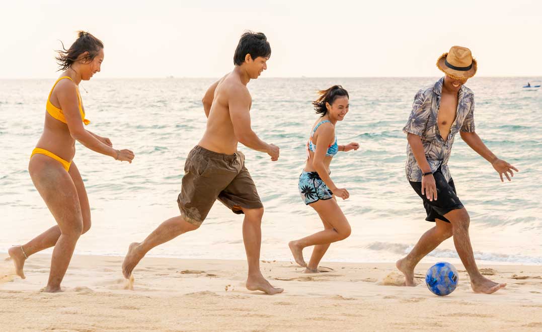Happy man and woman travel tropical beach on summer holiday vacation. Group of Asian people friends enjoy and fun outdoor active lifestyle travel at the sea and playing soccer on the beach at sunset.